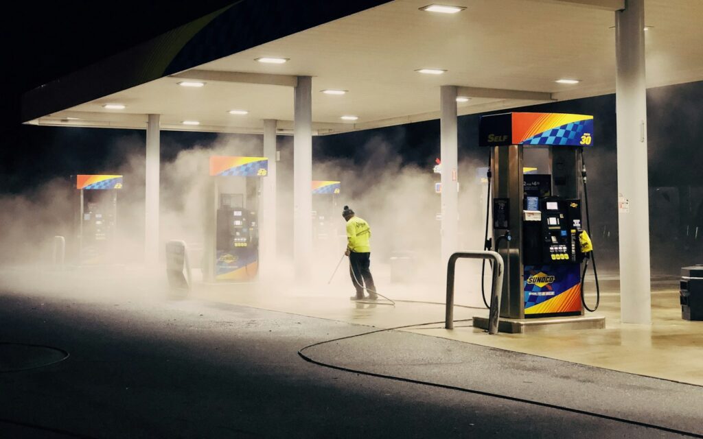 Worker pressure washing a gas station forecourt at night