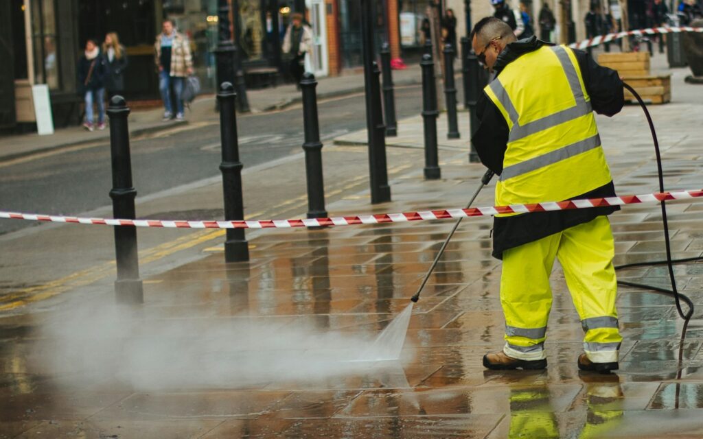 Worker in a yellow jacket using a gas pressure washer on a sidewalk