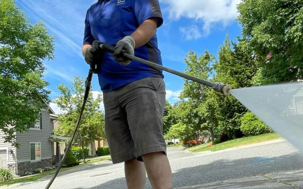 Technician pressure washing a residential driveway on a sunny day