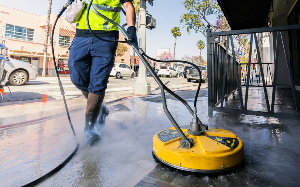 Pressure washing pro cleaning a storefront sidewalk with a surface cleaner