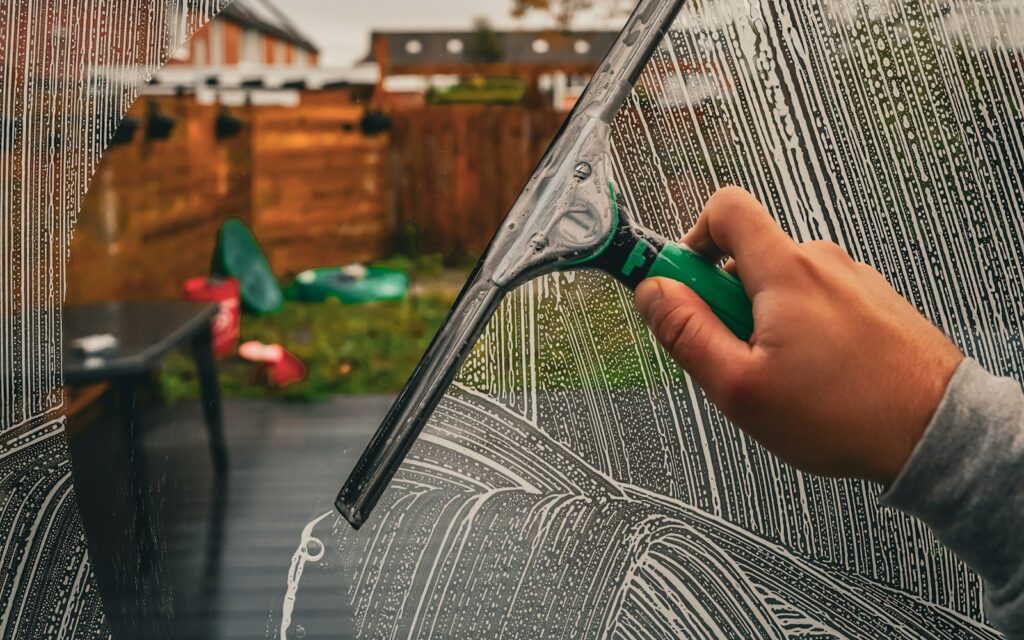 Window cleaner pulling a squeegee through soapy glass