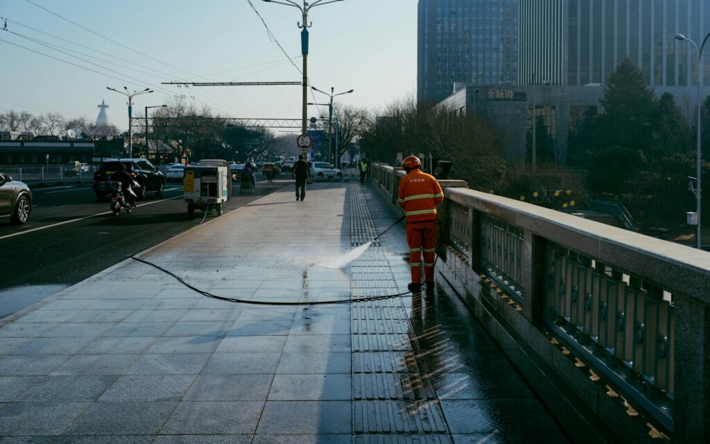 Worker in a safety vest washing a sidewalk with a high-pressure hose