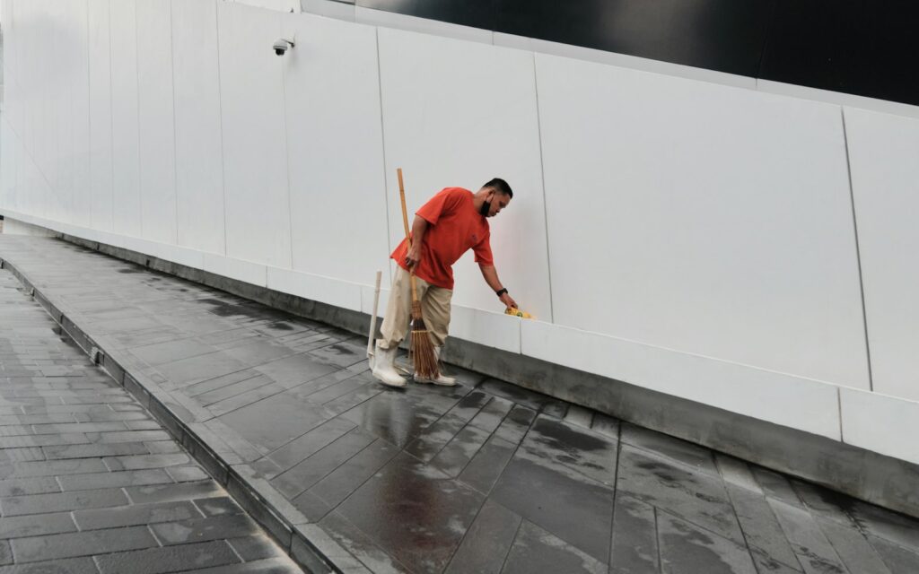 Worker spraying water to clean a white wall and pavement